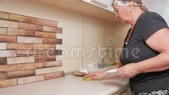 年长的女人擦桌布小心收集面包屑和碎片并投掷纯洁的房子概念视频的预览图