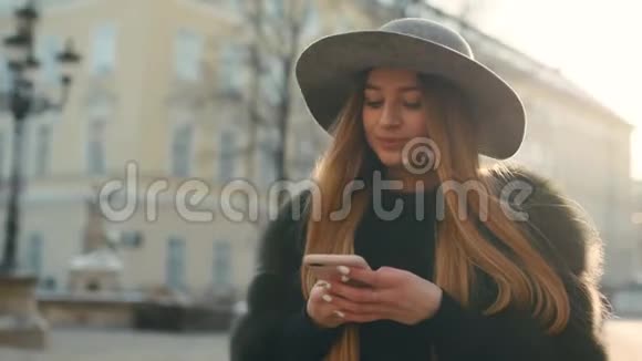 美丽的年轻女子站在市中心时在明亮的阳光下使用手机视频的预览图