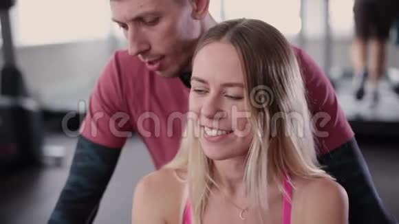 运动和有魅力的男人帮助一个漂亮的女人在健身房的地板上伸展视频的预览图