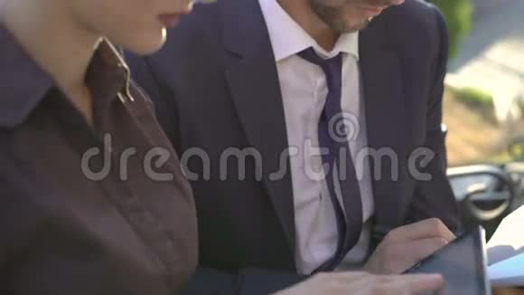 女人和男人用平板电脑工作在户外的长凳上笑4K视频的预览图