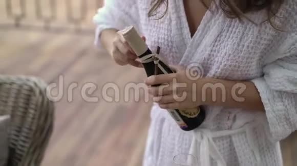 穿浴袍的年轻女子打开一瓶香槟视频的预览图