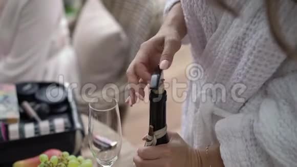 穿浴袍的年轻女子打开一瓶香槟视频的预览图