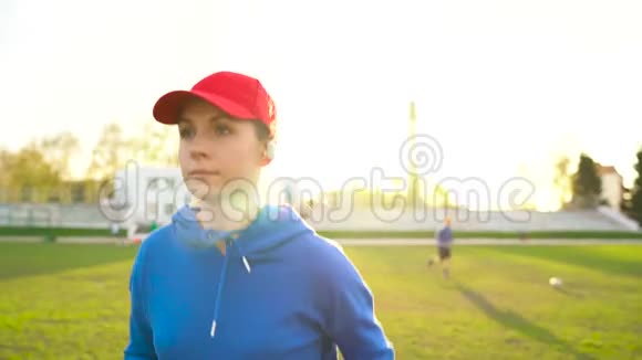 日落时分带无线耳机的女人穿过体育场视频的预览图