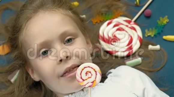 带棒棒糖的小女孩躺在蓝色的背景上特写肖像俯视图视频的预览图