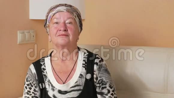 老女人认真地看着相机环顾四周家中沙发上一个忧郁女人的肖像视频的预览图