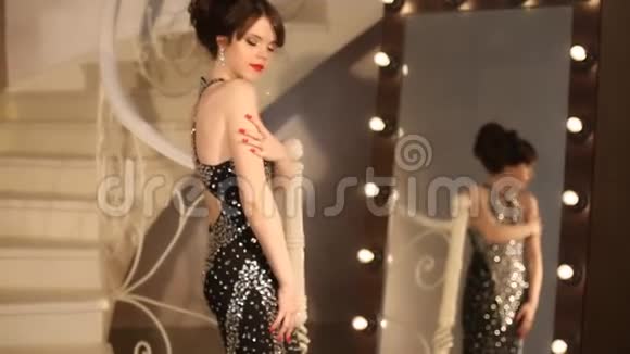 优雅的女士年轻的模特穿着豪华的黑色连衣裙可爱的女孩在镜子前灯泡在里面视频的预览图