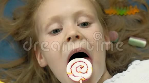 带棒棒糖的小女孩躺在蓝色的背景上特写肖像俯视图视频的预览图
