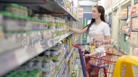 美丽的女人带着小儿子在超市购物年轻的母亲在市场上为孩子选择食物视频的预览图