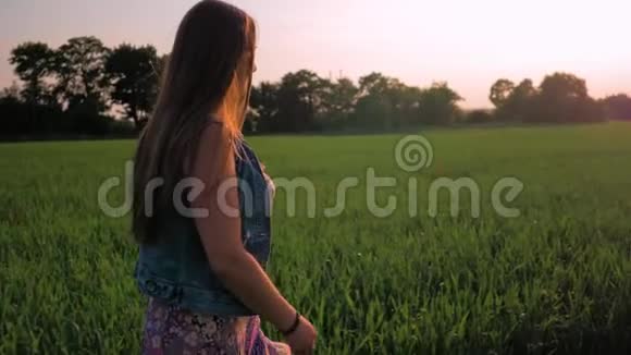 直发的年轻女孩正沿着一片绿色的田野走着夕阳西下中弹慢动作视频的预览图