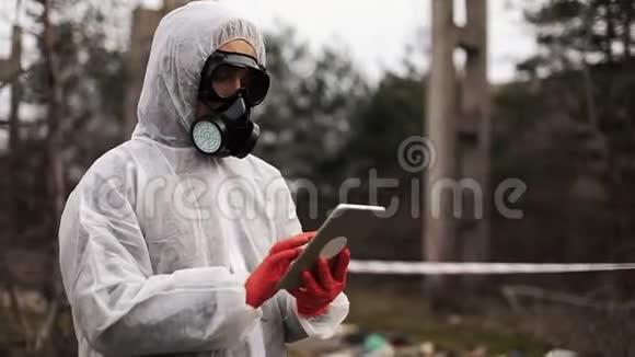 穿着生物危险服和防毒面具的人在被污染的土地上的平板电脑上记笔记视频的预览图