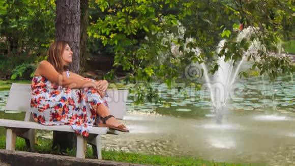 金发女孩坐在长凳上看着公园里的喷泉视频的预览图
