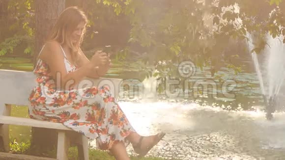 背光金发女郎坐在喷泉池的长椅上视频的预览图