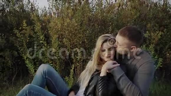 在秋天公园里一对年轻夫妇坐在草坪上互相欣赏视频的预览图