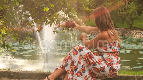 金发女孩坐在喷泉屏障上用Iphone自拍视频的预览图