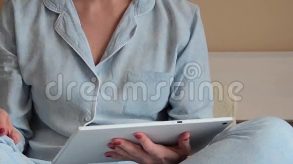 一位穿着蓝色睡衣的年轻女子坐在家里打字视频的预览图