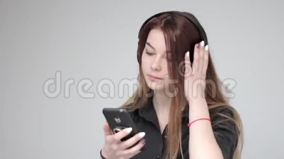 年轻漂亮的女士戴着黑色无线耳机使用智能手机浅色背景视频的预览图
