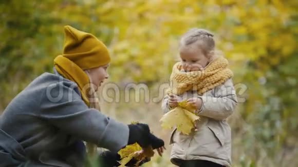 金发的小女儿和妈妈在秋天公园散步有有趣的和收集的叶子关闭视频的预览图
