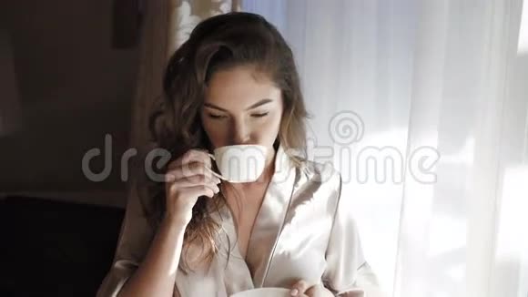 穿夜装的漂亮女孩在窗户附近喝了一杯咖啡视频的预览图