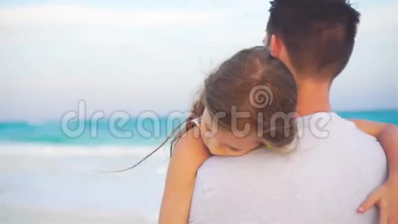 热带海滩上可爱的女孩和年轻的父亲晚上一家人在沙滩上视频的预览图