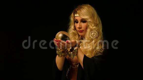 美丽的金发占星家女人透过水晶球看视频的预览图