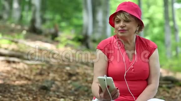 穿红色t恤戴红色帽子的女人在森林里听音乐视频的预览图