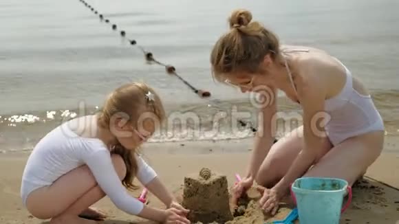 妈妈和女儿正在海滩上玩耍建造一座沙堡夏日阳光明媚假期视频的预览图