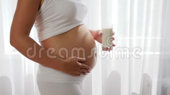 怀孕的女孩在大肚子的背景下拿着玻璃牛奶奶制品视频的预览图