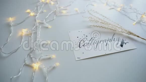 在光桌上的花环上用白色纸张上的斜体字书法特写明信片视频的预览图