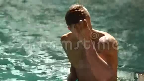年轻的裸胸男子正在游泳池游泳这家伙正牵着他的手头玩头发是在看视频的预览图