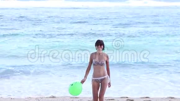 快乐的年轻苗条的女人穿着泳衣带着绿色的气球在海边奔跑慢动作地微笑着视频的预览图