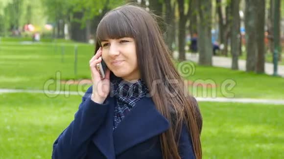 年轻女子在一个城市公园里用手机聊天背景上绿色的春草视频的预览图