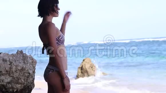 夏天的女孩穿着泳装的年轻女人住在靠近海洋和岩石的海滩上视频的预览图