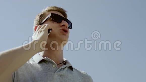 一个男人在天空背景下用手机说话的底视图视频的预览图