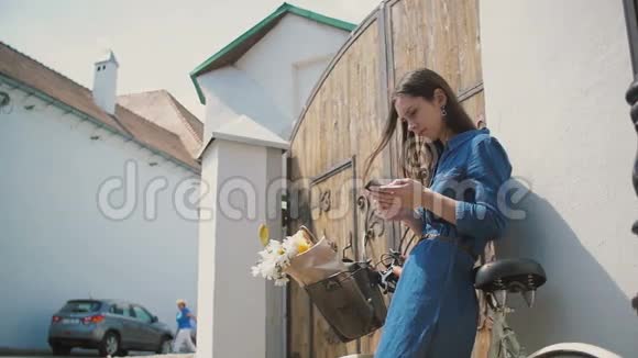 快乐的黑发女孩用她的智能手机用一辆自行车和一个篮子里的花在电话上谈笑风生慢悠悠视频的预览图