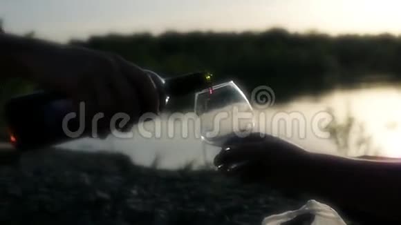 在夕阳和湖水的映衬下将红酒倒入大自然中的一个玻璃杯中慢动作视频的预览图