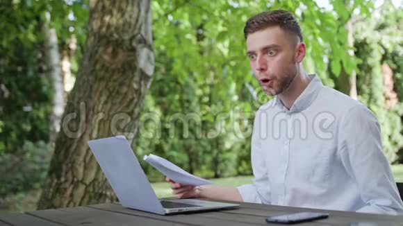 一个年轻人在公园里看书和使用笔记本电脑视频的预览图