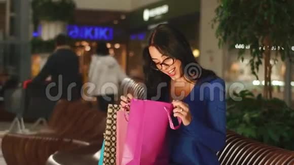 布鲁内特正坐在购物中心的长凳上拿着她的一个购物袋看着里面视频的预览图