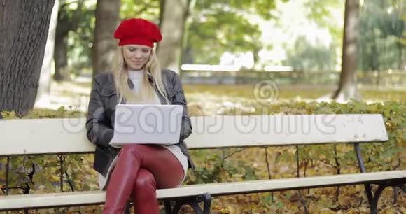 微笑的女人在公园里用笔记本电脑视频的预览图