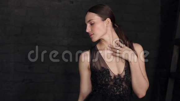 美丽的黑发女人穿着黑色的裙子摆姿势看着黑色墙壁背景上的相机视频的预览图