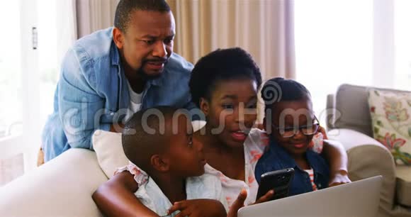 家长和孩子在沙发上使用笔记本电脑和智能手机视频的预览图