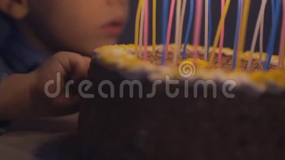 体贴的男孩试着用蛋糕和蜡烛做手指霜男孩在慢动作的生日蛋糕上吹蜡烛视频的预览图