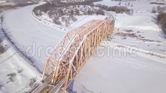 铁路桥梁和铁路轨道为列车交通在冰冻河流上的冬季景观无人机景观悬挂列车视频的预览图