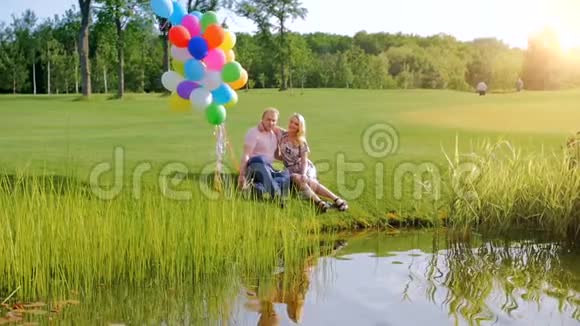 一对美丽的年轻情侣坐在河边的慢镜头视频的预览图