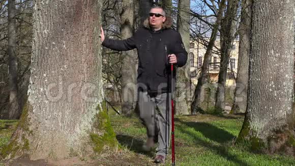 徒步旅行者用手杖在公园的树旁锻炼腿视频的预览图