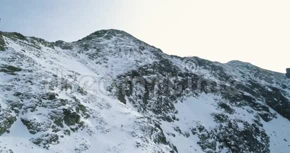 冬天的雪山上空中落后登山滑雪者向上攀登雪覆盖着群山视频的预览图