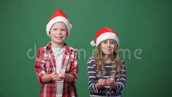 可爱的男孩和女孩戴着圣诞帽扔纸屑视频的预览图