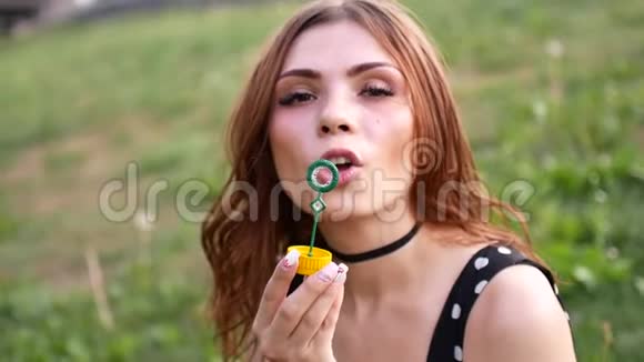 女孩吹肥皂泡年轻漂亮的女人坐在公园的草地上玩泡泡慢速视频视频的预览图