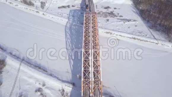 无人机视图列车在铁路桥上越冬河行驶通过冰冻的河流训练悬索桥的交通视频的预览图