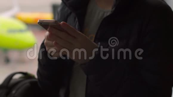 一名年轻女子在机场一扇大窗户前使用智能手机的特写镜头视频的预览图