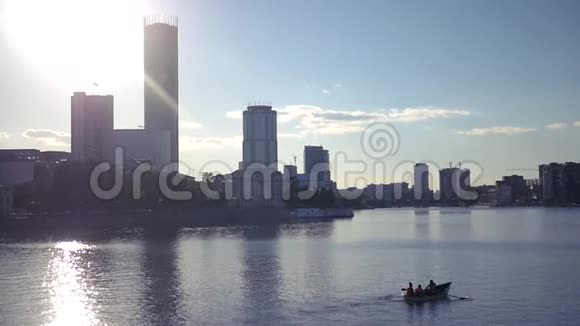 城市景观的背景下一个阳光湖突出和船在桨上一个男人和一个女孩漂浮在上面视频的预览图